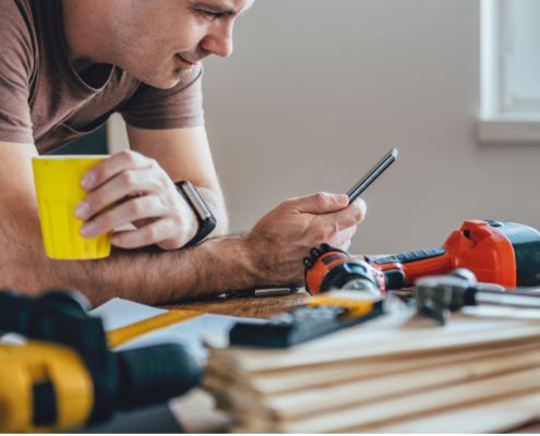 Man holding a cup while looking at his phone with power tools in the background