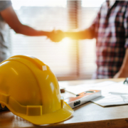 Picture focuses on a hard hat while in the background 2 men are shaking hands